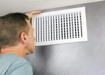 Mature man examining an outflow air vent grid and duct to see if it needs cleaning. One guy looking into a home air duct to see how clean and healthy it is.