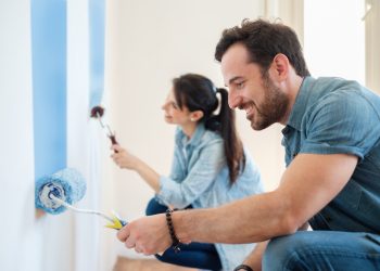 Young couple painting walls in their new house, do it yourself concept