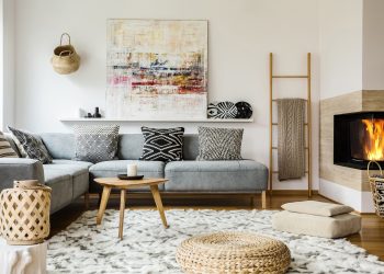 Wooden table next to grey corner settee in warm living room interior with painting and fireplace. Real photo