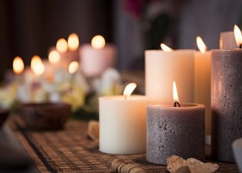 Closeup of burning candles spreading aroma on table in a spa room. Beautiful composition with grey and white candles for spa treatment. Zen and relax concept.