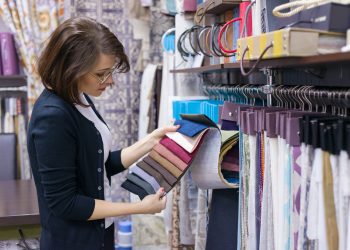 Woman designer, decorator chooses fabrics for curtains, pillows, embroidering fabrics, carpets in the textile show room