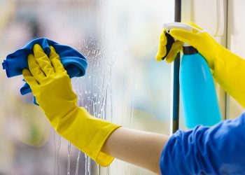 Female hand in yellow gloves cleaning window pane with rag and spray detergent. Cleaning concept