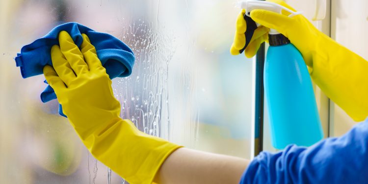 Female hand in yellow gloves cleaning window pane with rag and spray detergent. Cleaning concept