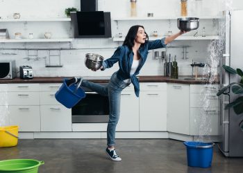 Full length view of shoked woman in jeans dealing with water leak in kitchen