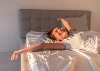 Happy woman lying in comfortable foam latex mattress bed in luxury hotel enjoying relax weekend getaway jumping in bed. Enjoying Asian woman with open arms in freedom.