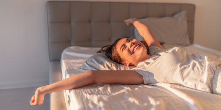 Happy woman lying in comfortable foam latex mattress bed in luxury hotel enjoying relax weekend getaway jumping in bed. Enjoying Asian woman with open arms in freedom.