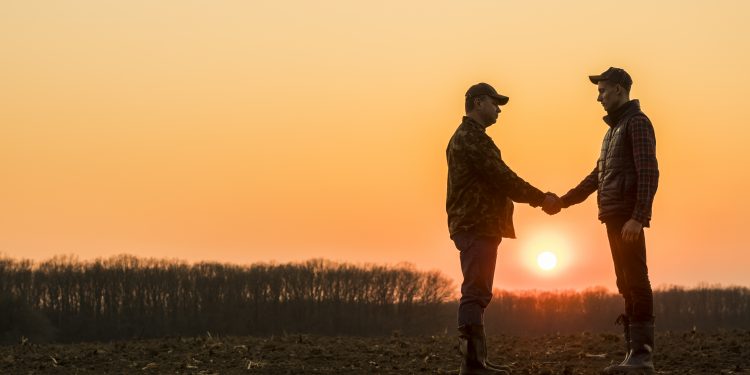 Two farmers on the field shake hands at sunset.