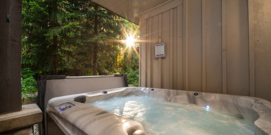 A outdoor hot tub near a forest with a sunburst coming through the trees