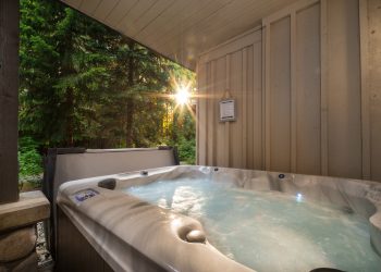 A outdoor hot tub near a forest with a sunburst coming through the trees