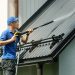 man standing on ladder and cleaning house metal roof with high pressure washer