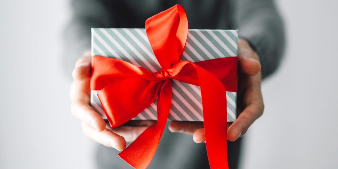 Young man holding gift with red ribbon. Closeup