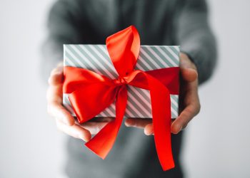 Young man holding gift with red ribbon. Closeup