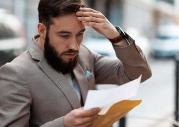 Big debt alert. A shocked man reads a court letter. Death of a loved one, increased mortgage payments.