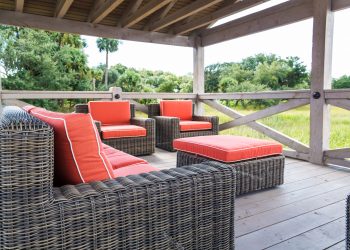 A patio in the tropics with brown rattan furniture and orange cushions