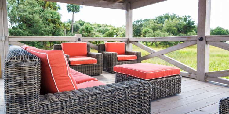 A patio in the tropics with brown rattan furniture and orange cushions
