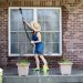 Housewife standing on a patio washing the windows of her house with a hose attachment as she spring-cleans the exterior at the start of the new spring season