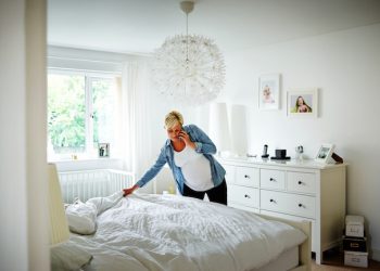 Pregnant woman talking on mobile phone and making bed at home