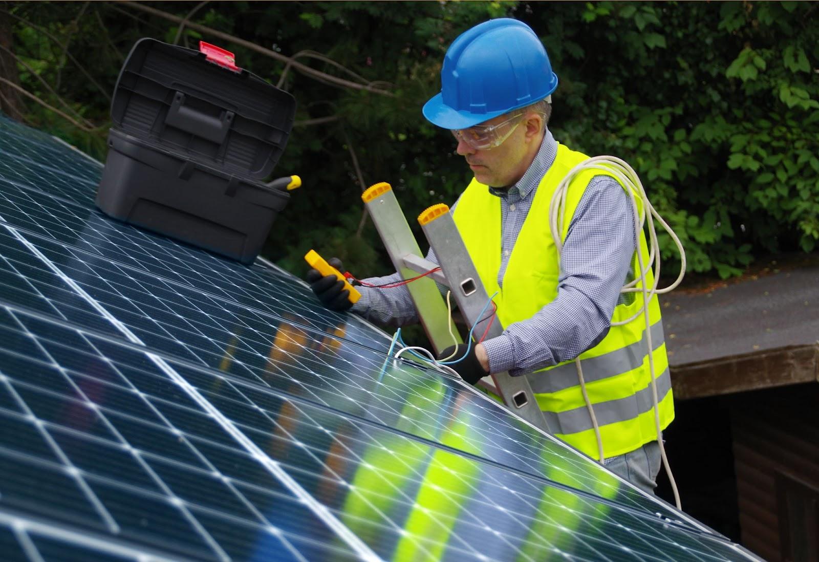 A person wearing a hard hat and safety vest working on a solar panel Description automatically generated with low confidence