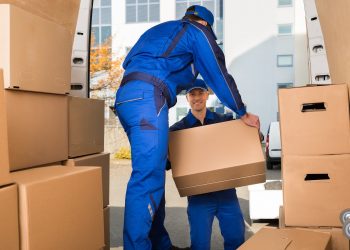 Full length of young male movers carrying sofa outside truck on street