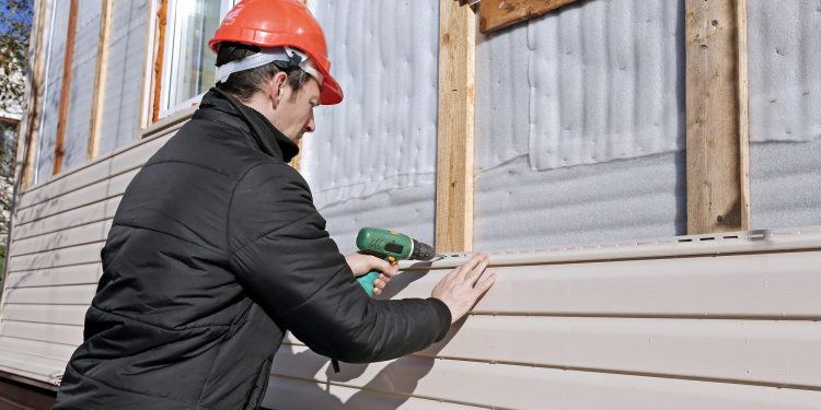 A worker installs panels beige siding on the facade of the house