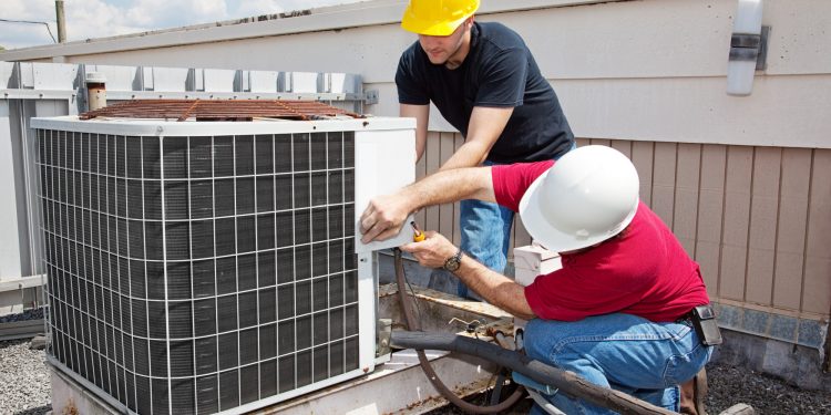 Two workers on the roof of a building working on the air conditioning unit.