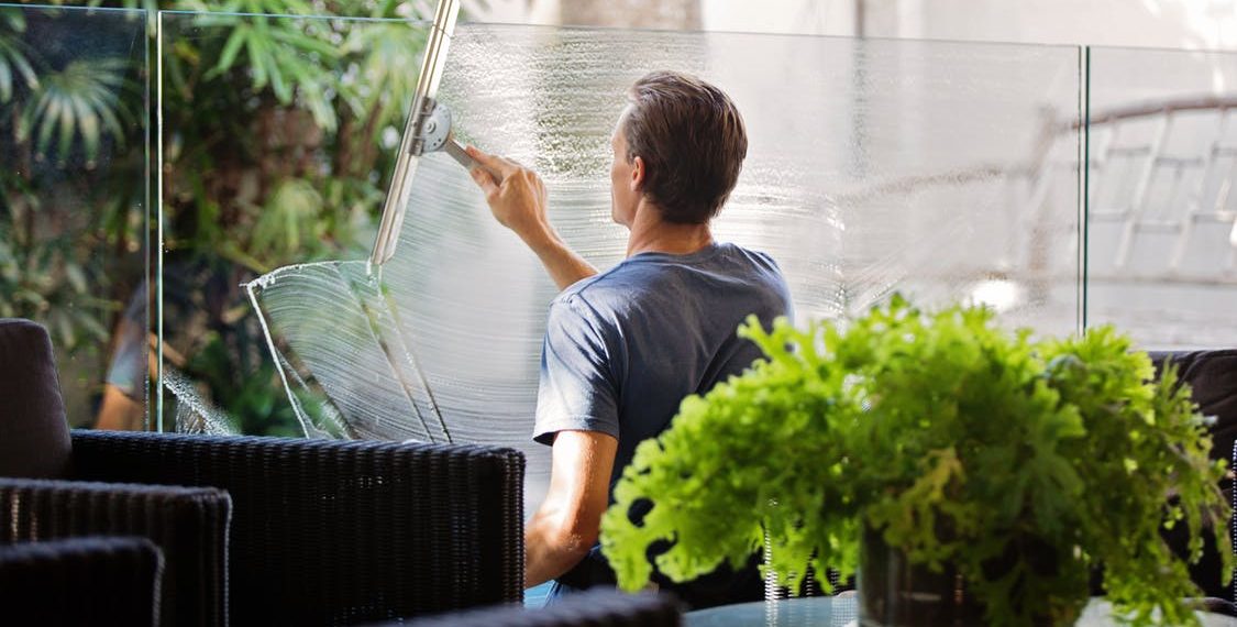 Man in Gray Shirt Cleaning Clear Glass Wall Near Sofa