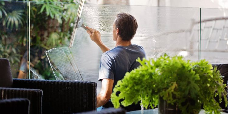 Man in Gray Shirt Cleaning Clear Glass Wall Near Sofa