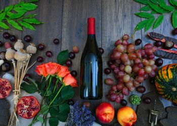 Wine Bottle Beside Grapes, Roses and Several Fruits on Brown Wooden Surface