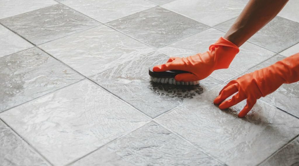 Hand of man wearing orange rubber gloves is used to convert scrub cleaning on the tile floor.