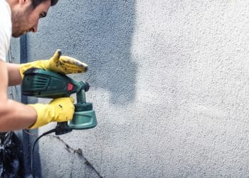 Man painting a grey wall, renovating exterior walls of new house